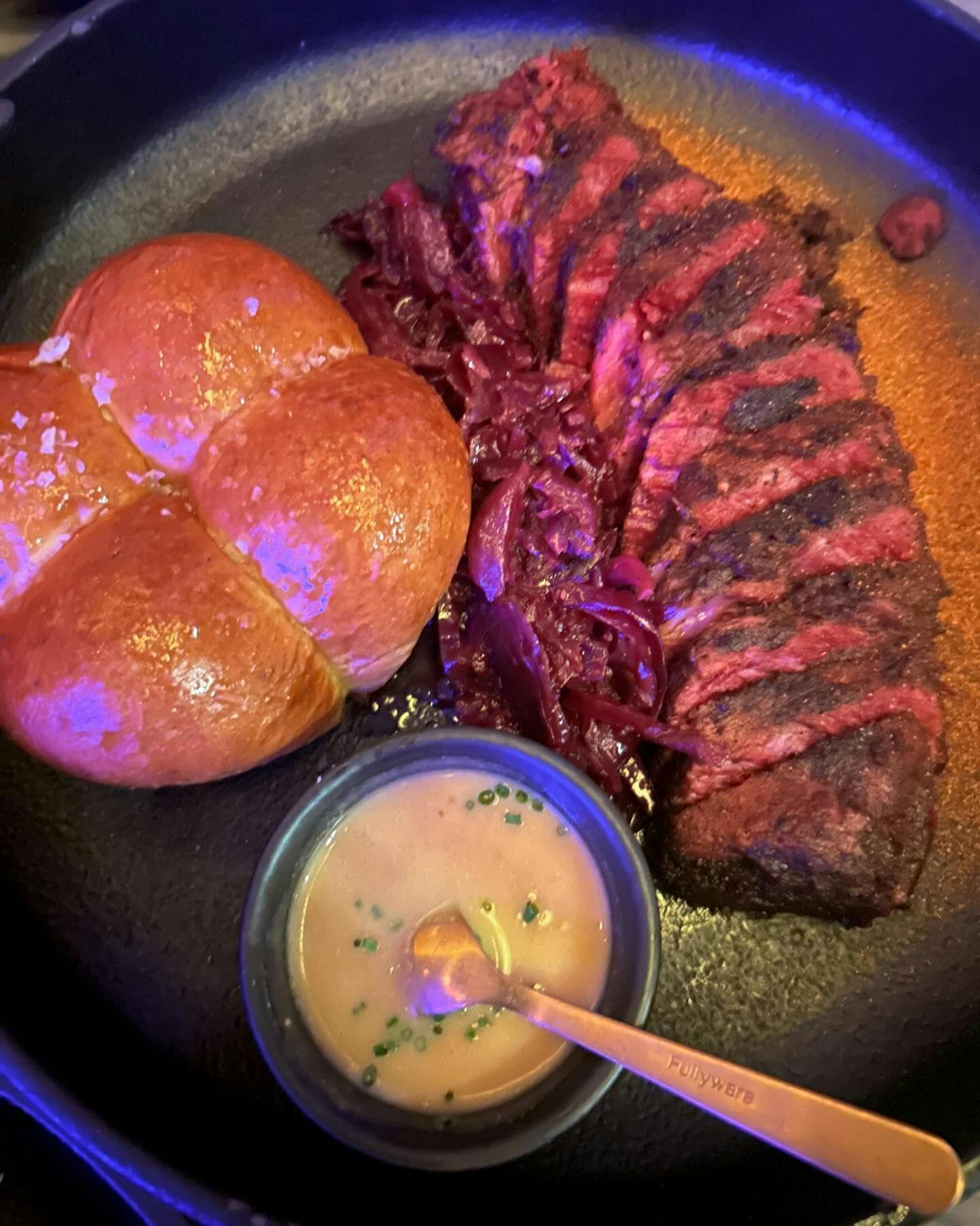 Perfectly grilled steak sliced and served alongside golden brioche rolls and braised red cabbage, complete with a side of creamy sauce, embodying the fine dining experiences accessible with Booked in New York.