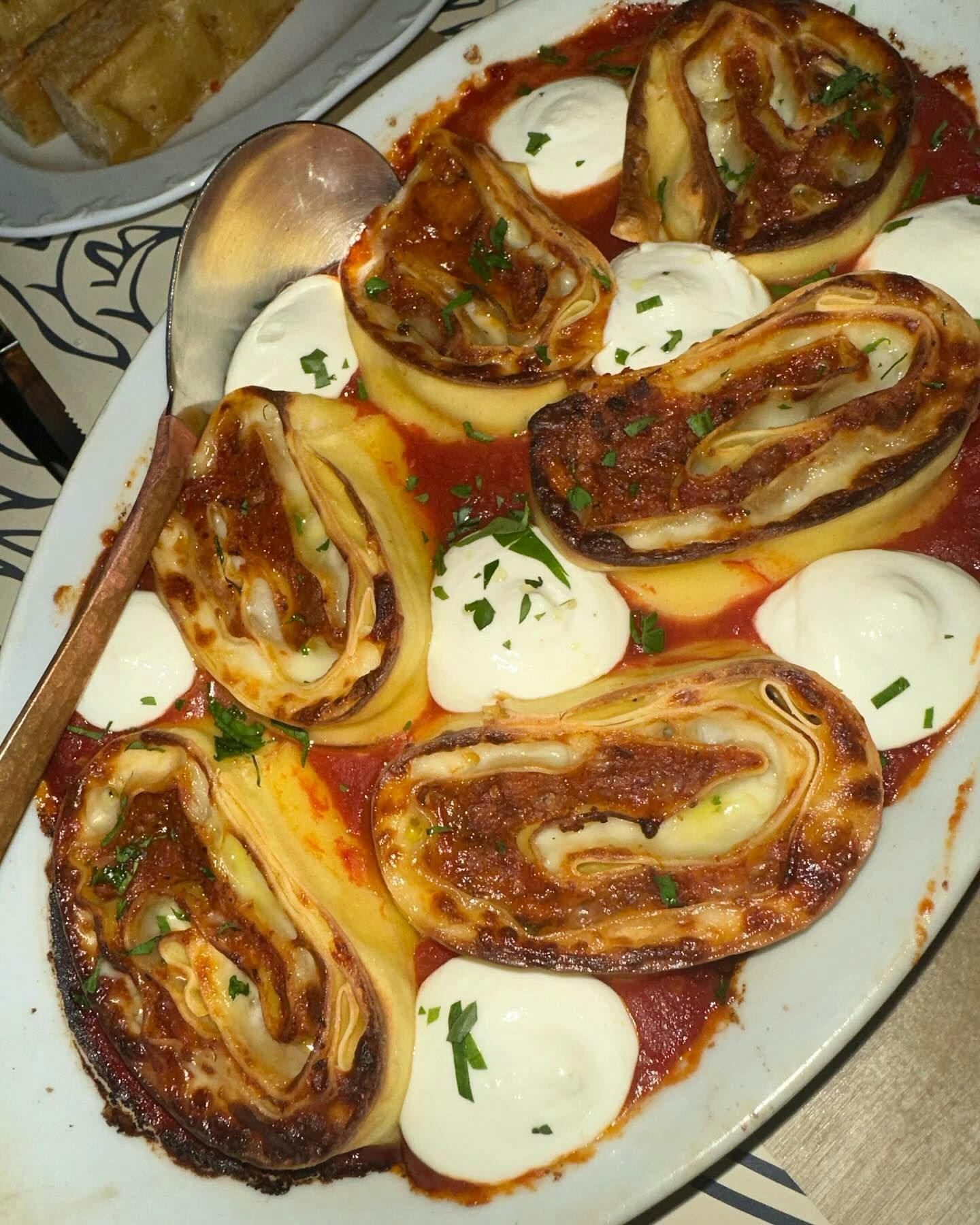 Savory rolled pasta in a tomato sauce adorned with dollops of cream and sprinkled with herbs, served on a decorative plate as part of a refined dining experience available through Booked in New York.