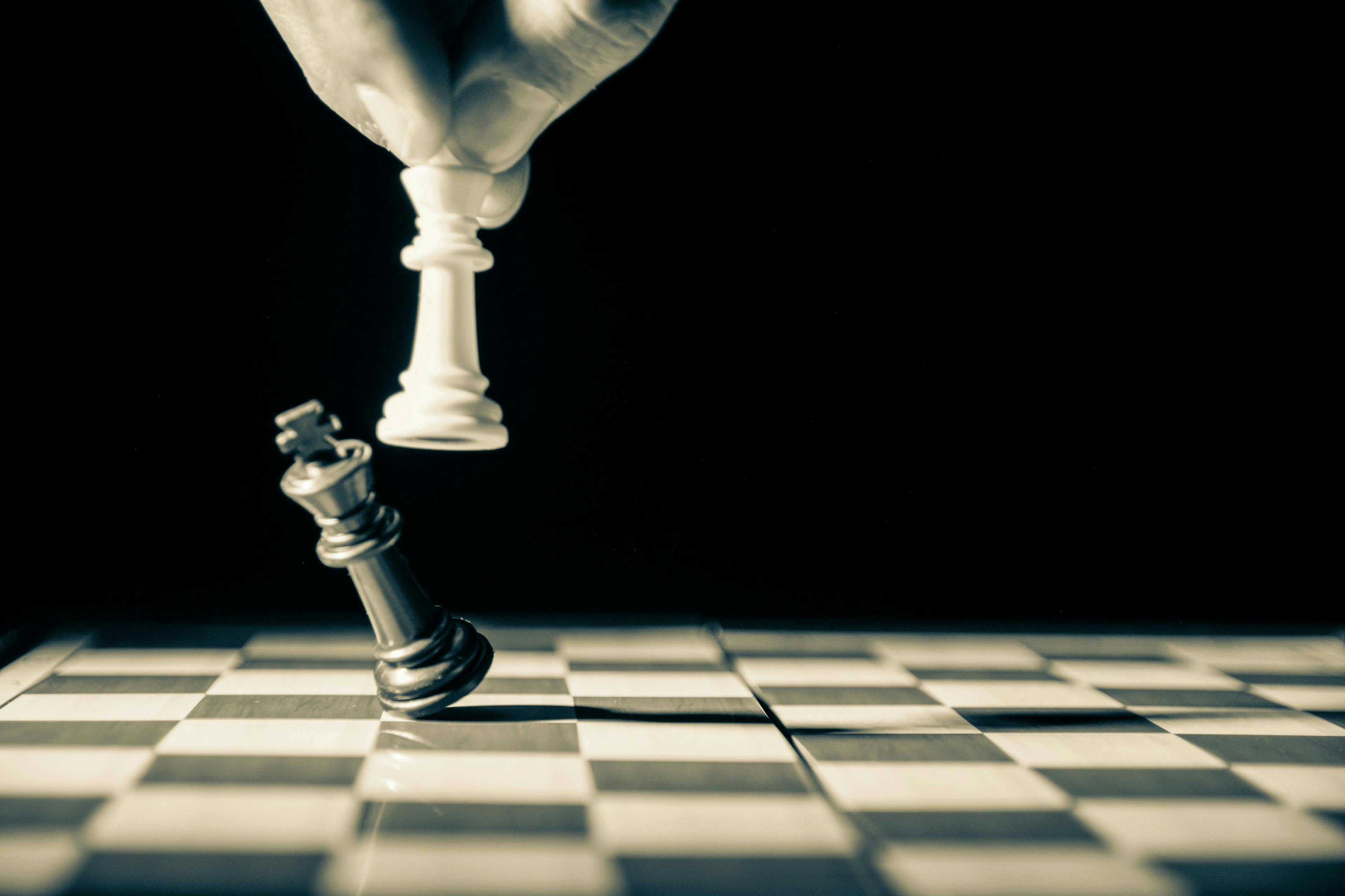 A dramatic chess scene capturing the decisive moment of checkmate with a hand confidently moving the white queen piece, indicating victory over a fallen black king, symbolizing strategic triumph and foresight.