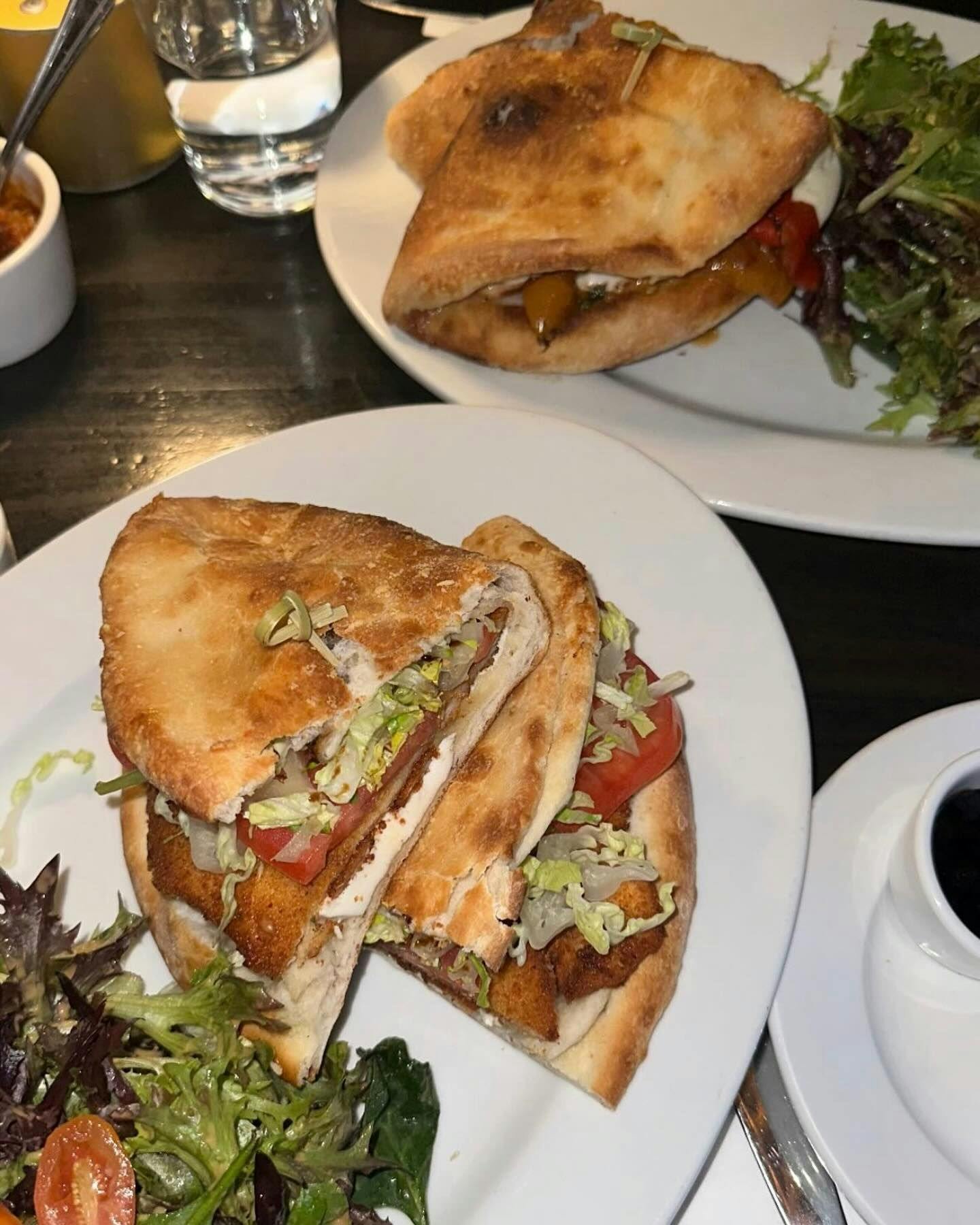 Grilled chicken sandwich cut in halves, stuffed with fresh lettuce and tomato, served with a side of mixed green salad, representing the casual yet quality dining options available in New York through Booked.
