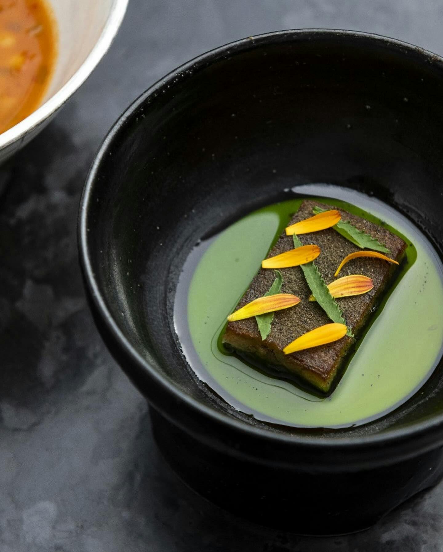 A modern artistic dessert with matcha flavors, presented on a sleek black dish and garnished with vibrant orange petals and green leaves, highlighting the innovative cuisine found in New York’s premier restaurant reservation marketplace.