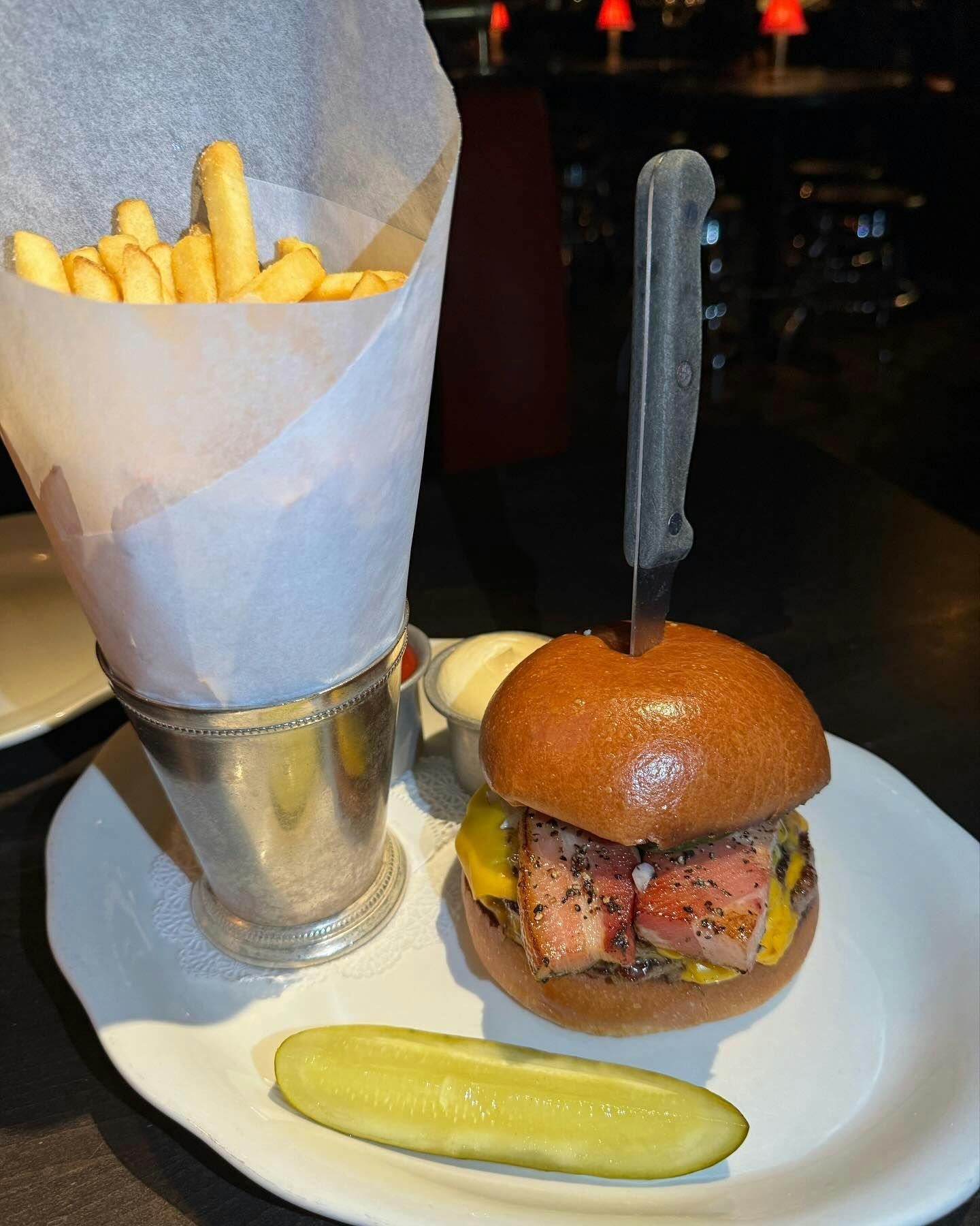 A gourmet burger with a perfectly seared patty and melty cheese on a brioche bun, accompanied by a cone of golden fries and a crisp pickle, ready to be enjoyed in one of New York's premium dining establishments available through Booked.