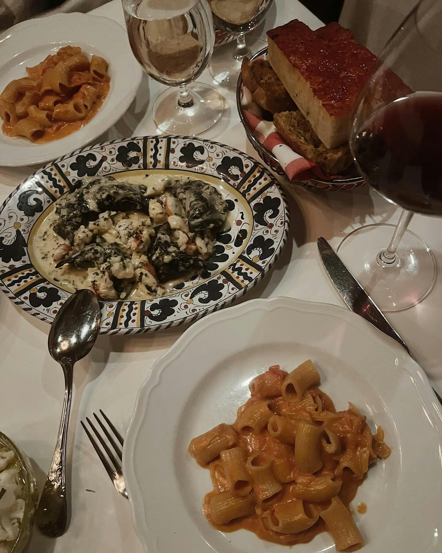 A table adorned with a variety of Italian pasta dishes, including rigatoni in a creamy tomato sauce and a rich spinach pasta, accompanied by a crisp glass of wine, showcasing the exquisite dining experiences found in New York's restaurants with Booked.